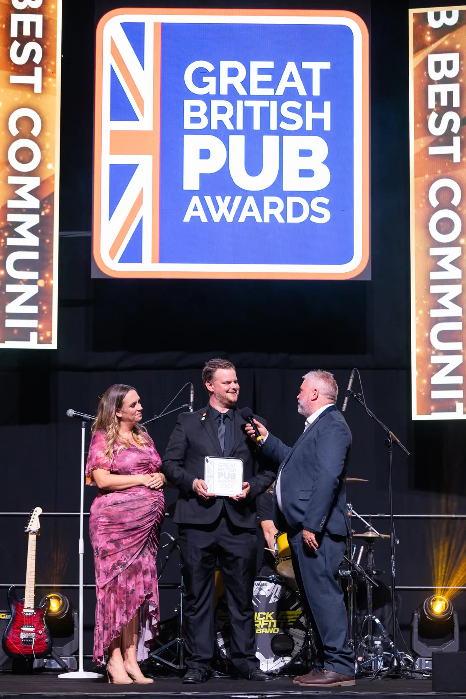 The Swan's award being presented on stage, with a microphone held out, beneath the Great British Pub Awards logo and Best Community Pub banners